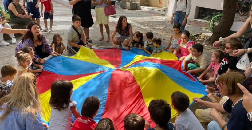 krāsains apaļš izpletnis, pie tā bērni un skolotāji