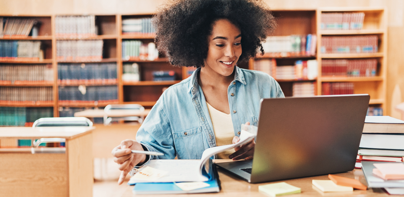 Studente bibliotēkā mācās pie atvērta datora